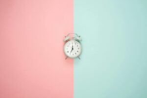 A vintage round clock on a split pastel pink and blue background.